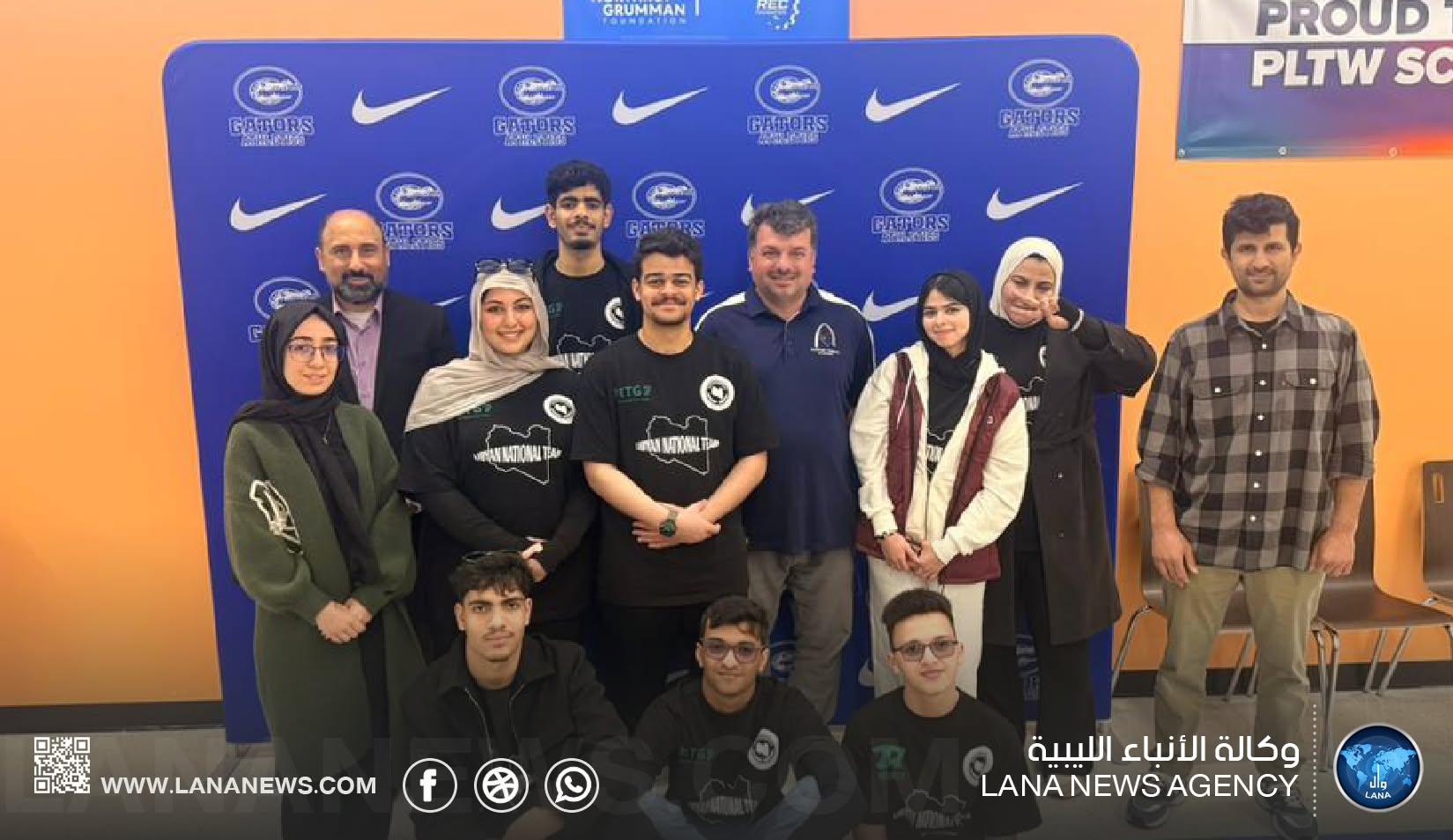 صورة جماعية لطلاب بقمصان سوداء تحمل عبارة Libyan National Team مع عدد من الكبار أمام خلفية زرقاء.