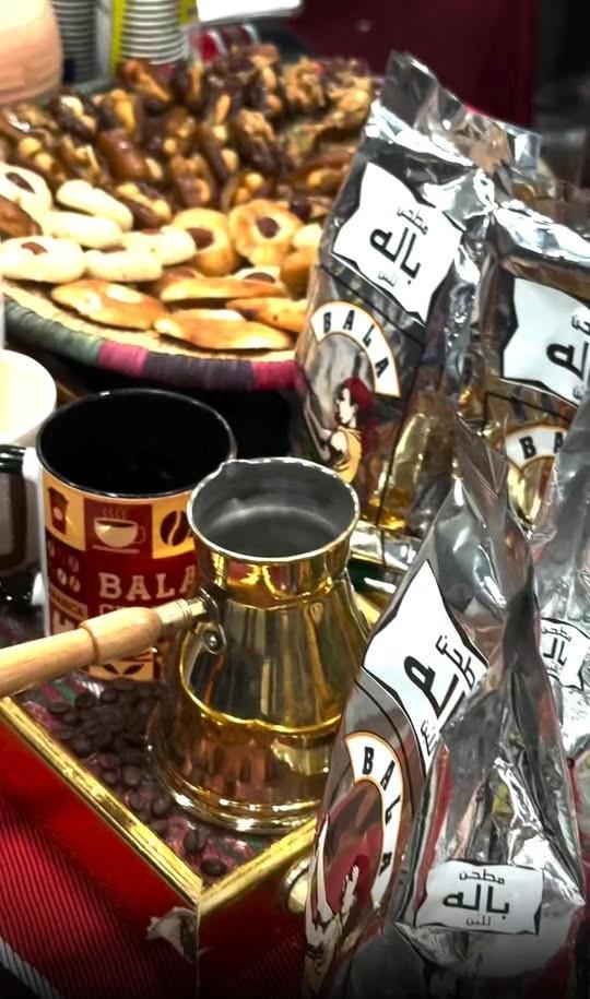 طاولة عليها إبريق قهوة نحاسي وكوب باله وأكياس قهوة وحلويات وتمر.