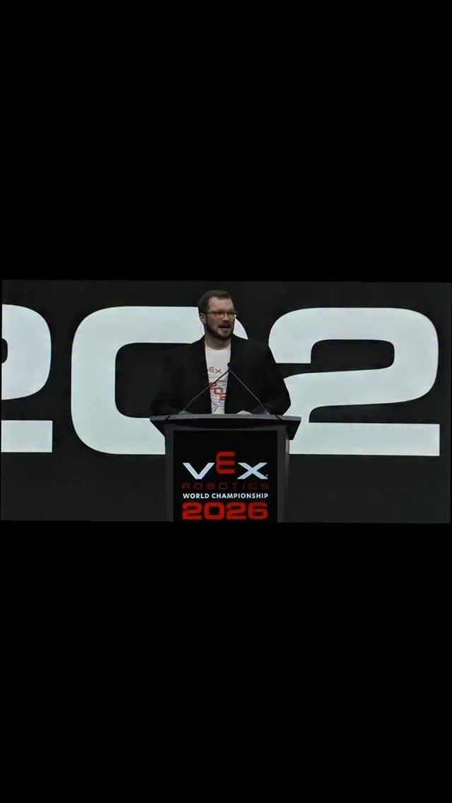 متحدث على منصة بطولة العالم للروبوتات VEX 2026 أمام لافتة كبيرة تحمل الرقم 2026