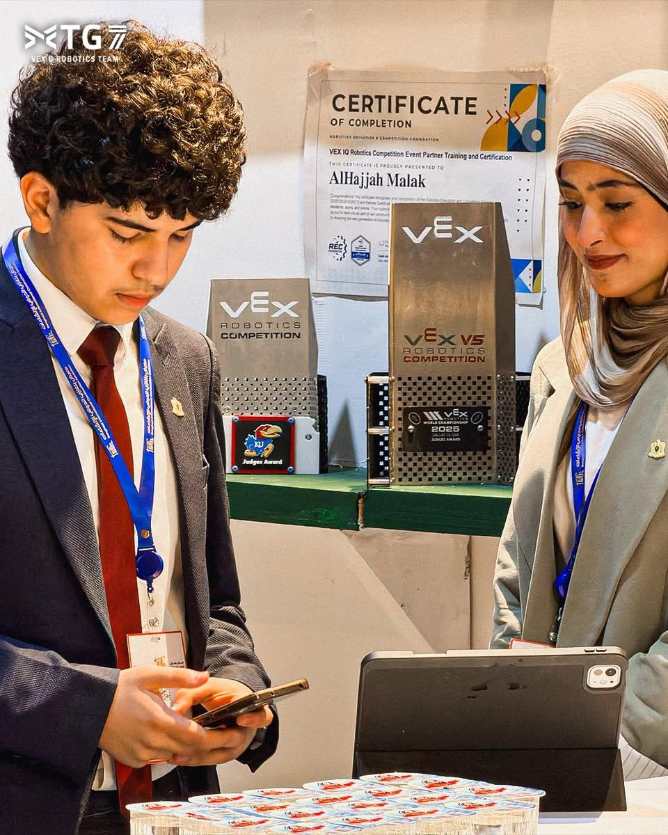 شاب وشابة عند طاولة الجناح، وخلفهما كؤوس VEX وشهادة معلقة