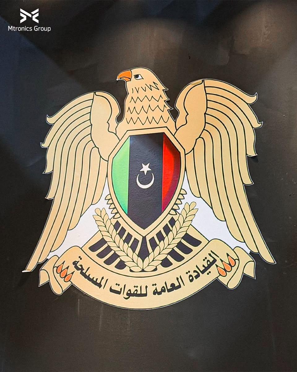شعار القيادة العامة، نسر ذهبي يحمل درعاً بألوان العلم الليبي، على جدار داكن
